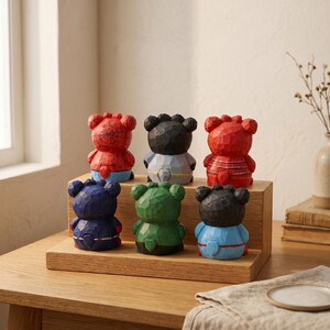 Puede incluir: Colecci&oacute;n de seis figuras de osos tallados en varios colores, incluyendo rojo, azul, verde y negro. Los osos se exhiben en una estanter&iacute;a de madera, con algunos detalles que sugieren temas de superh&eacute;roes. Las figuras est&aacute;n sobre una mesa de madera.