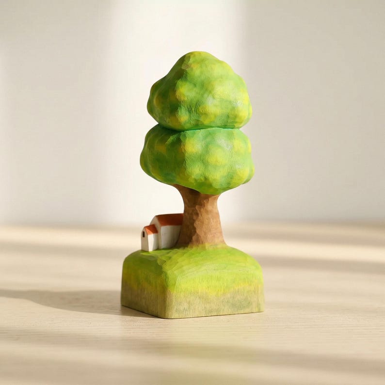 May include: A hand-carved wooden figurine featuring a tall tree with a rounded, textured green canopy and a brown trunk. At the base of the tree sits a small white house with a red roof, all resting on a square, light green grassy platform.