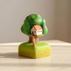 May include: A hand-carved wooden sculpture featuring a green tree with a small white house nestled in its branches. The house has an orange roof and a wooden staircase leading down to a green base. The entire piece has a textured, painted finish.