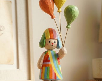 Estatueta artesanal de madeira representando uma menina com dopamina, balões coloridos, decoração lúdica para mesa ou prateleira.