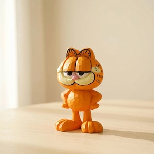May include: Orange Garfield figurine with a carved wood appearance. The figurine has a grumpy expression, with its arms at its sides. The cat's eyes are closed, and it has a pink nose and a cream-colored mouth. The figurine is standing on a light-colored surface.