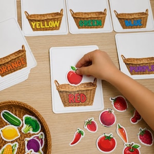 Puede incluir: Tarjetas educativas de clasificación con ilustraciones de cestas de mimbre etiquetadas con colores como amarillo, verde, azul, naranja, morado y rojo. Un recorte de manzana roja se coloca sobre la tarjeta de la cesta roja, junto a otros recortes de frutas y verduras.