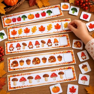 May include: A set of five rectangular educational pattern strips featuring autumn-themed illustrations including pumpkins, apples, broccoli, maple leaves, gnomes, mushrooms, hedgehogs, and acorns, accompanied by matching square tiles for sequence completion.