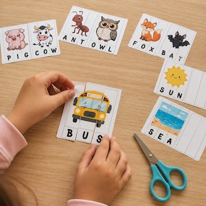 Puede incluir: Tarjetas educativas con ilustraciones de dibujos animados de animales, un autobús, el sol y el mar con las letras correspondientes debajo de cada imagen. Las tarjetas están segmentadas en tiras verticales. Se incluyen unas tijeras azul claro.