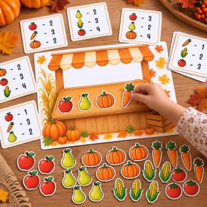 Op de afbeelding: Een educatief telspel met herfstthema, bestaande uit een grote geïllustreerde marktstalmat, diverse kleine kaartjes met rekenopgaven over fruit en groenten, en talloze losse uitgesneden afbeeldingen van appels, peren, pompoenen, wortels en maïs.