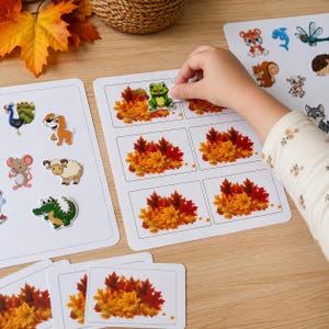 May include: A set of white activity sheets featuring colorful animal stickers and illustrations of autumn leaves in shades of red, orange, and yellow. The sheets include various cartoon animals like a frog, dog, mouse, sheep, and alligator.