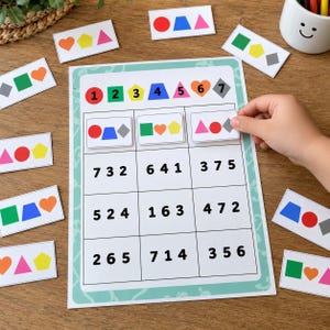 Puede incluir: Una hoja de actividades educativas imprimible que presenta una cuadrícula de números y un conjunto de tarjetas pequeñas con formas geométricas coloridas, incluyendo círculos, cuadrados, triángulos, corazones y pentágonos para ejercicios.
