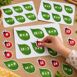 Puede incluir: Juego educativo de matemáticas con tarjetas rectangulares blancas que muestran hojas verdes con ecuaciones de suma y resta, junto con pequeños recortes de mariquitas rojas que exhiben números correspondientes a los problemas.