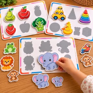 Può includere: Tre tavole educative rettangolari bianche con illustrazioni colorate di frutta, verdura, veicoli, giocattoli e animali. Ogni tavola contiene ritagli e pezzi corrispondenti, tra cui un elefante blu, un leone e una rana.
