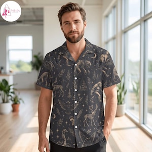 May include: A dark gray short-sleeve button-down shirt featuring a repeating pattern of gold-colored skeletal animals, including a deer, a bird, and a creature resembling a sasquatch, interspersed with stars, crescent moons, and pine trees.