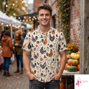 May include: A short-sleeve button-down shirt with a cream background featuring a repeating pattern of roosters, pumpkins, witch hats, and stars. The shirt has a notched collar and is worn with dark denim jeans in an outdoor market setting.