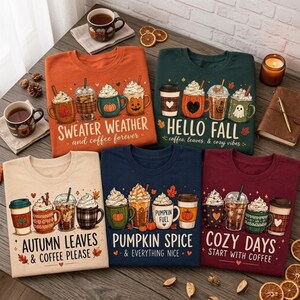 May include: Five t-shirts in orange, dark green, cream, navy, and maroon, each featuring graphic prints of coffee cups and seasonal text like "Sweater Weather," "Hello Fall," "Autumn Leaves," "Pumpkin Spice," and "Cozy Days" with autumn motifs.