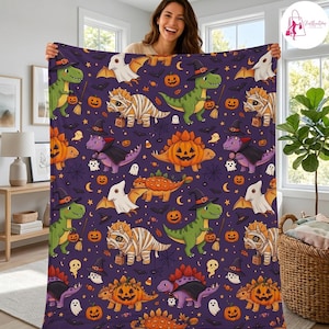 May include: A purple fleece blanket featuring a repeating pattern of cartoon dinosaurs dressed in Halloween costumes, including mummies, vampires, and witches, interspersed with orange jack-o'-lanterns, white ghosts, and black spiderwebs.