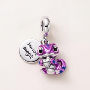 Può includere: Un ciondolo in argento a forma di lucertola smaltata viola e blu che tiene un piccolo cuore in argento. Il pezzo include un disco rotondo in argento inciso con il testo You are magic e un gancio per l'attacco a un bracciale o una collana.