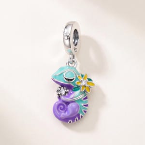 Könnte beinhalten: Ein Charm-Anhänger aus Sterlingsilber in Form eines eingerollten Chamäleons mit leuchtend türkisfarbener und violetter Emaille. Das Chamäleon ist mit einer kleinen gelben Blume und zwei klaren Steinen verziert, der Stempel 925 ist auf der Öse.