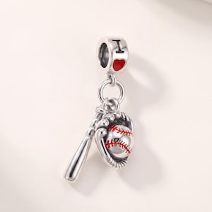 May include: A silver charm featuring a baseball bat and a baseball glove holding a ball with red stitching. The top bail is engraved with the letter I and a red heart symbol. The charm is crafted from polished silver with detailed metalwork.