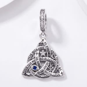 May include: A silver charm pendant featuring a triquetra knot design with engraved text including BE KIND, SPEAK WITH LOVE, and HONOR YOUR WORD. The piece is accented with a small blue stone, a clear crystal star, and a crystal-encrusted bail.