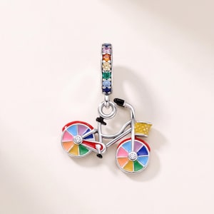 Op de afbeelding: Een zilveren bedel in de vorm van een fiets met veelkleurige emaille wielen en een geel mandje. Het oogje is versierd met een verticale rij kleine, ronde, veelkleurige edelstenen. Het fietsframe is zilverkleurig met een heldere steen.