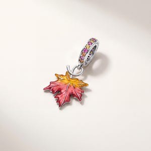Può includere: Un charm in argento a forma di foglia d'acero con una finitura in smalto sfumato che passa dal rosso all'arancione e al giallo. Il passante è decorato con una fila di piccole pietre preziose rotonde e multicolori rosa, arancioni e gialle.