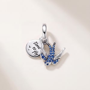 Puede incluir: Un charm de plata con forma de golondrina incrustada con pequeños cristales azules y un disco circular de plata grabado con el texto Time to fly. El charm incluye una anilla de plata pulida en la parte superior para sujetarlo a una pulsera.