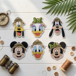 May include: Six embroidered patches featuring the faces of Pluto, Daisy Duck, Goofy, Mickey Mouse, Donald Duck, and Minnie Mouse, each wearing a tan and green safari hat. The patches are arranged in two rows on a white wooden surface.