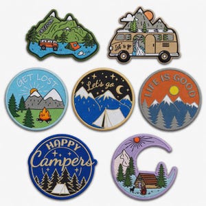 May include: A collection of embroidered camping patches with various designs. The patches feature images of mountains, forests, tents, and a camper van. Text includes "Freedom", "Get Lost", "Let's go", "Life is Good", and "Happy Campers".