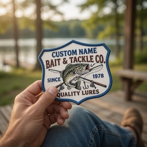 Könnte beinhalten: Ein individueller Angelaufnäher in Schildform mit einer detaillierten Illustration eines Fisches, gekreuzten Angelruten und dem Text "Custom Name Bait & Tackle Co. Since 1978 Quality Lures". Der Aufnäher hat einen blauen Rand.