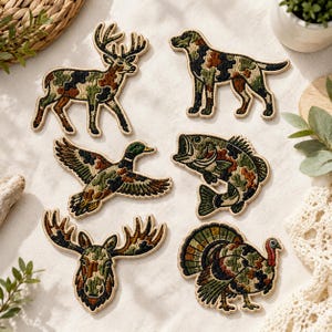 May include: A set of six embroidered patches featuring a deer, a dog, a flying duck, a fish, a moose head, and a turkey. Each patch is filled with a camouflage pattern in shades of green, brown, black, and tan with a light beige border.