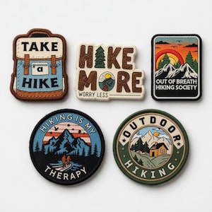 May include: Five embroidered patches with hiking themes. One patch says "Take a Hike" with a backpack graphic. Another says "Hike More, Worry Less." Other patches feature mountain and outdoor scenes with text like "Out of Breath Hiking Society."