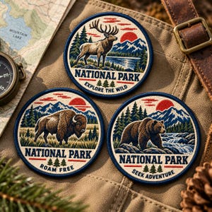 May include: Three circular embroidered patches featuring National Park themes. One shows an elk, one a bison, and one a bear, all set against mountains, forests, and red suns. Each patch includes the text National Park and unique phrases.