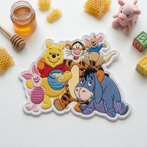 May include: A large embroidered patch featuring the characters Winnie the Pooh, Piglet, Tigger, Roo, and Eeyore. The design shows Pooh holding a blue honey pot, with the other characters gathered around him in a colorful, detailed stitched illustration.