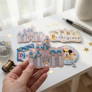 May include: A collection of embroidered fabric patches featuring a pink and blue castle, a Disneyland logo, and a circular Mickey Mouse icon. The patches are detailed with intricate stitching and vibrant colors, showcasing iconic theme park imagery.