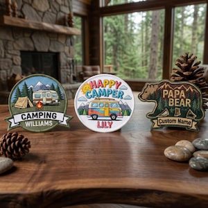 Könnte beinhalten: Drei Camping-Patches auf einem Holztisch. Ein Patch zeigt einen Camper und den Text "Camping Williams". Ein anderes sagt "Happy Camper" mit einem Wohnmobil. Das dritte ist ein Bär mit "Papa Bear" und Platz für einen individuellen Namen.