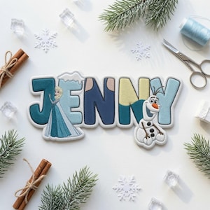 Puede incluir: Un parche bordado personalizado con el nombre JENNY en letras de bloque, con tonos azules y amarillos. La letra J muestra un personaje rubio con vestido azul, y la letra Y presenta un mu&ntilde;eco de nieve blanco con una nariz de color naranja.