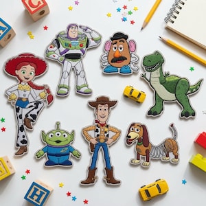 May include: A collection of seven embroidered fabric patches featuring characters from the Toy Story franchise, including Woody, Buzz Lightyear, Jessie, Mr. Potato Head, Rex, Slinky Dog, and an Alien, arranged on a white surface with scattered toys.
