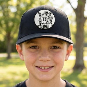 Może przedstawiać: Czarna czapka bejsbolowa z okrągłą naszywką przedstawiającą gracza w baseball trzymającego kij. Na naszywce widnieje nazwisko "Smith" i numer "23" na koszulce gracza. Czapka jest noszona przez osobę.