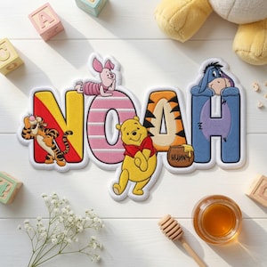 May include: A custom embroidered wall hanging featuring the name NOAH in large, colorful letters. The letter N features Tigger, the O features Piglet, the A features Winnie the Pooh with a honey pot, and the H features Eeyore. The design is white-bordered.