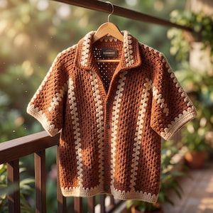 May include: A short-sleeved crochet button-down shirt featuring a brown and cream color scheme. The garment has a collared neckline, a vertical striped pattern created by the crochet stitch, and a small rectangular label reading HANDMADE.