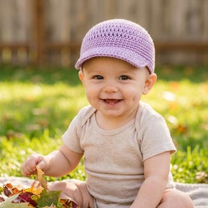 Peut inclure: Une casquette de baseball crochetée en violet clair avec une calotte arrondie et une visière courte et rigide. Le chapeau présente un motif de mailles tissées et texturées sur toute la surface, offrant un aspect structuré et doux.