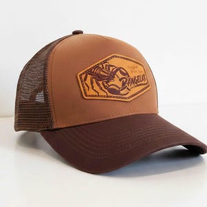 Könnte beinhalten: Braune Trucker-Mütze mit dunkelbraunem Schirm und Mesh-Rückseite. Die Mütze hat einen Lederaufnäher mit einer Krabbenillustration und dem Wort "RANGELAB".