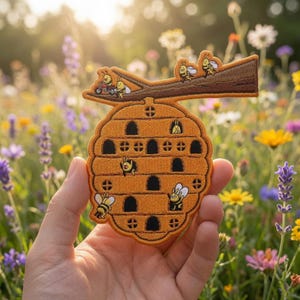 May include: An embroidered patch shaped like a golden beehive hanging from a brown tree branch. The hive features multiple dark arched openings and small windows, with several cartoon bees depicted in various activities around the structure.