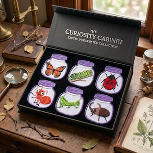 May include: A black box set titled "The Curiosity Cabinet" containing six embroidered insect patches. Each patch depicts a different insect inside a jar with a purple lid. Insects include a butterfly, caterpillar, ladybug, ant, grasshopper, and beetle.