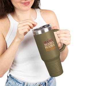 May include: Olive green travel mug with a black lid and handle. The mug features the word "MAMA" stacked four times in pink and orange lettering. The mug has a silver rim and a clear straw.