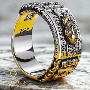 May include: A silver and gold-toned ring with intricate detailing. The ring features a raised gold-colored snake head and engraved patterns. The inside of the ring is gold, with the text "2502" visible. The ring is from the "Vorenza SilverAtelier" brand.