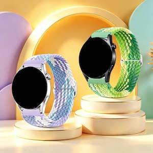 May include: Two smartwatches with round black screens and braided elastic bands. One watch has a silver casing and a lavender, blue, and white patterned strap. The other watch has a black casing and a green and yellow gradient braided strap.