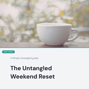 May include: A white ceramic coffee cup sits on a wooden surface, with a blurred background of light and shadow. The text "The Untangled Weekend Reset" is displayed below, promoting a guide for resetting over a weekend.