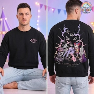 May include: A black long-sleeve sweatshirt featuring a small purple eye graphic on the front left chest. The back displays a large, colorful graphic of multiple cartoon characters with the text "we still have each other" and "- Digital Circus Finale".