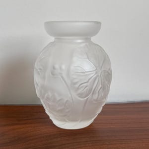 May include: A frosted glass vase with a rounded body and a wide, smooth rim. The exterior surface features a relief pattern of large, stylised leaves and small berries, creating a textured, matte appearance across the entire translucent vessel.