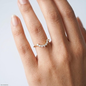 May include: A gold ring with a curved design, set with multiple small, clear gemstones. The ring is on a finger, showcasing its delicate and elegant appearance. The ring's design is a modern take on a classic style.