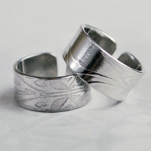 Puede incluir: Dos anillos de plata con un diseño texturizado y estampado. Los anillos están apilados uno encima del otro.